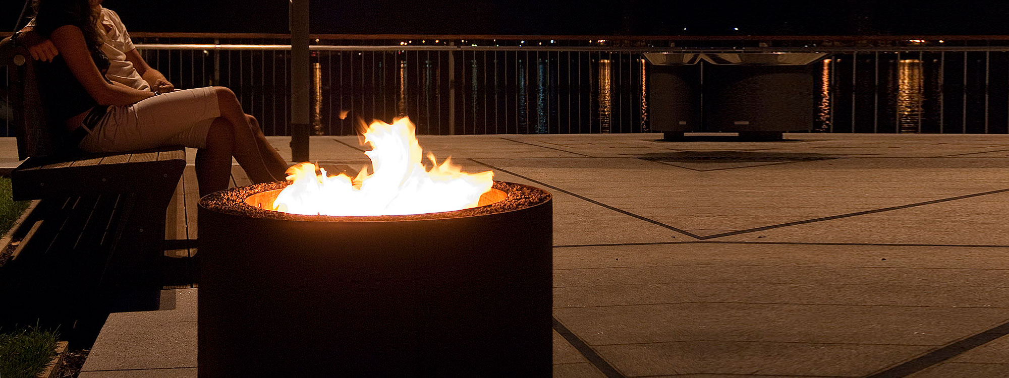 Image of couple enjoying the warmth of AK47 Mangiafuoco small fire pit at night on shore of lake.