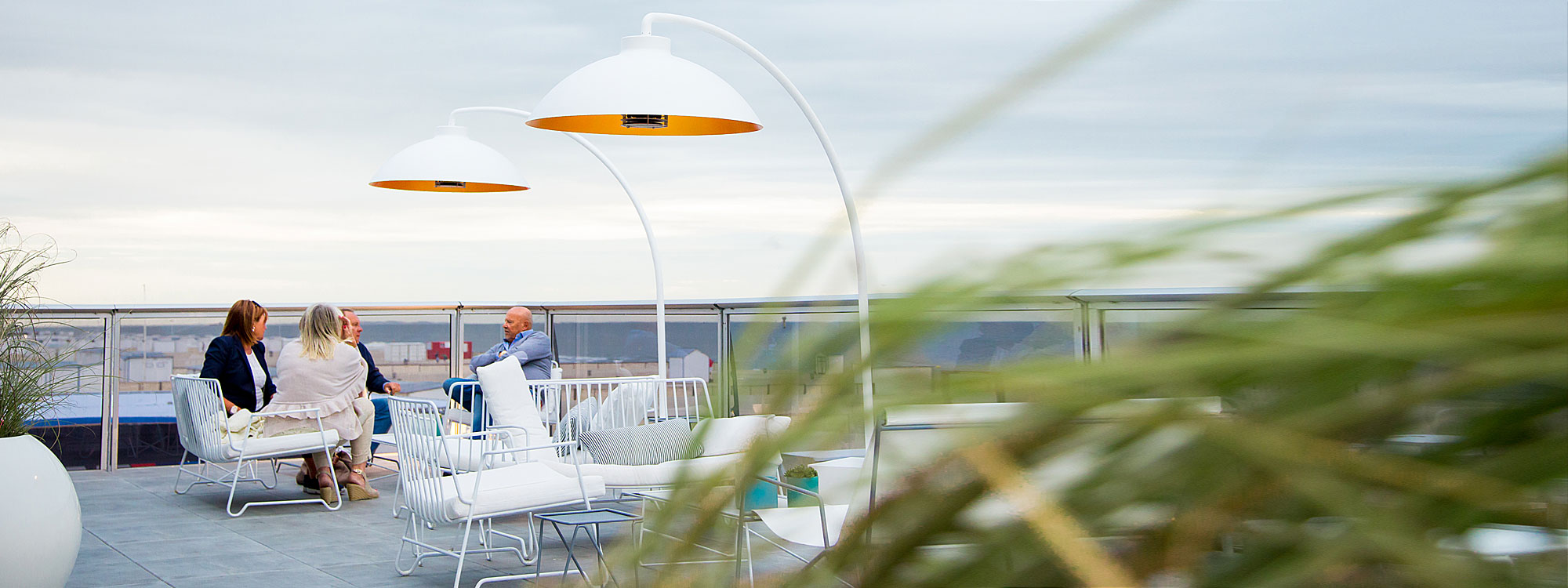 Image of pair of white Heatsail Dome cantilever heaters on rooftop with folks chatting on lounge furniture in background