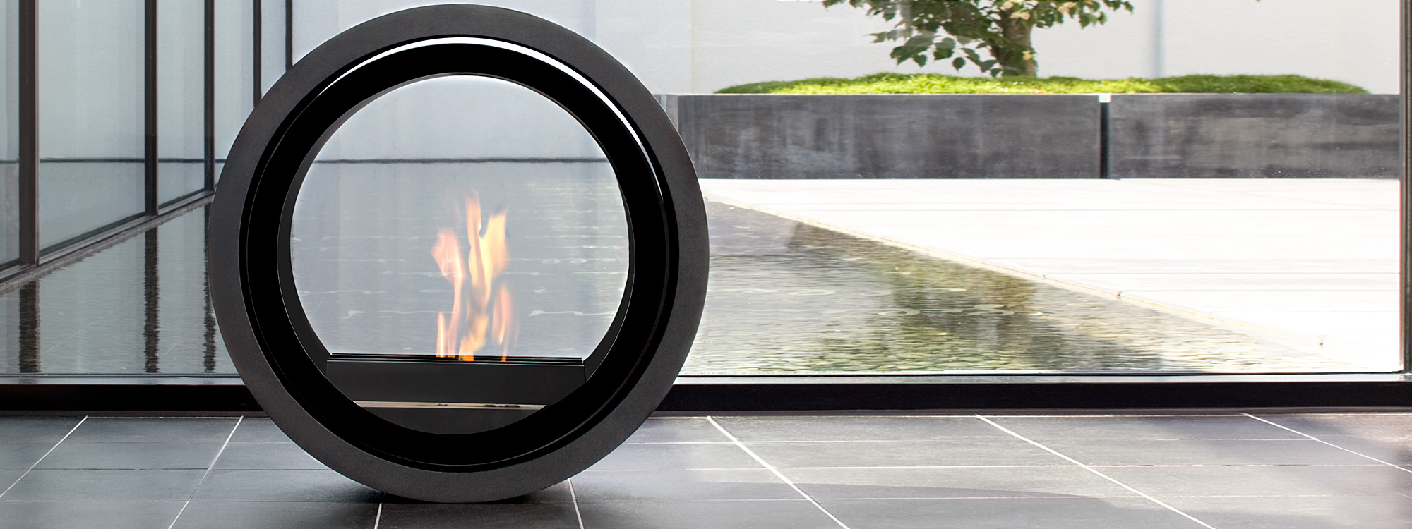 Image of flickering flames within Conmoto Roll flueless fire with tranquil water feature outside in background