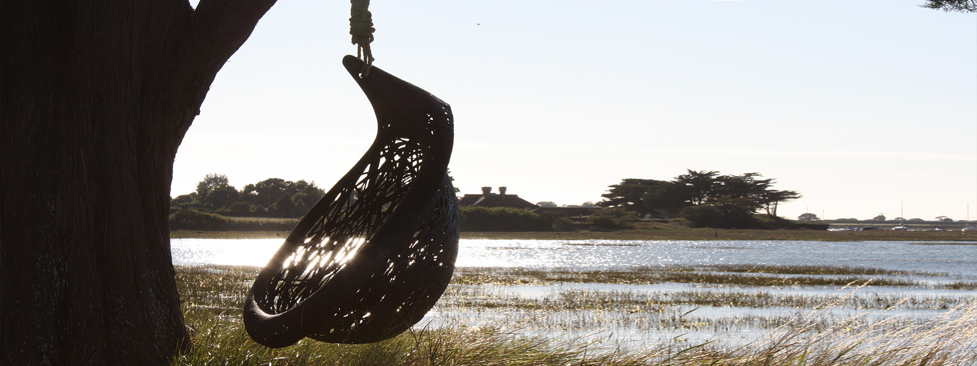 Image of silhouette of Bios Lucid single swing seat by Unknown Nordic, with sparkling water of Chichester Harbor in the background