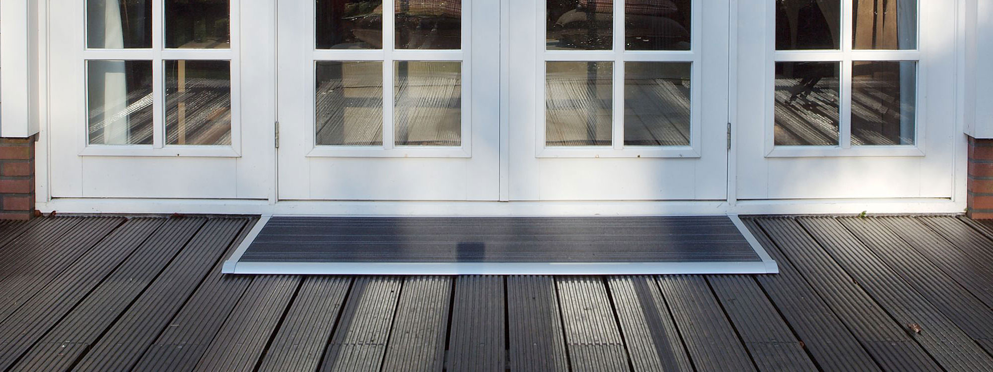Image of large anodized silver RiZZ The New Standard doormat shown on wooden decking outside white doorway