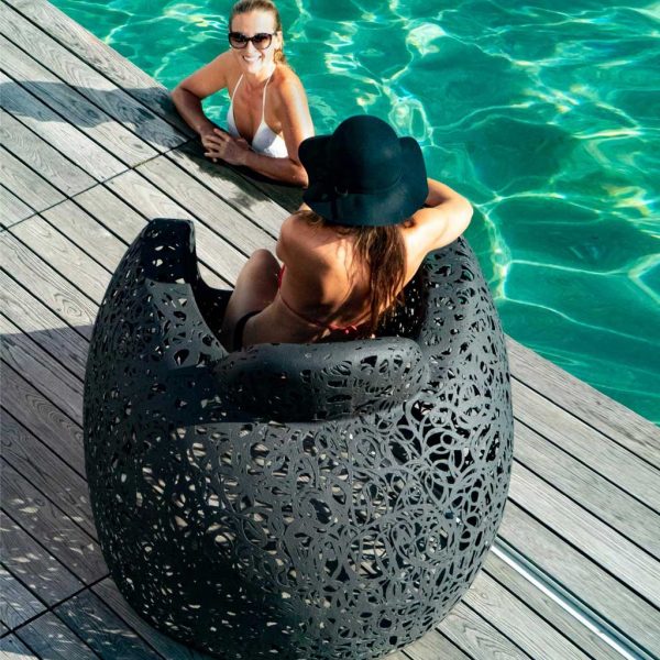 Image of woman sat in black Stellar garden chair by Unknown Furniture, talking to another woman in swimming pool