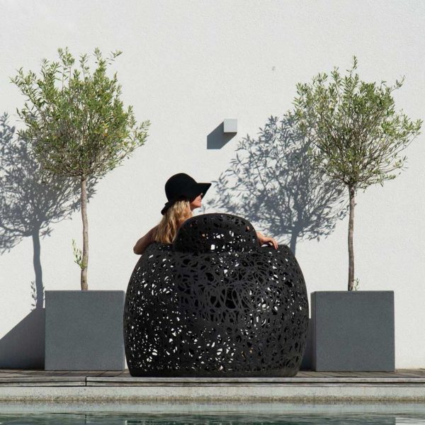 Image of back of Stellar black garden armchair by Unknown Nordic furniture, shown in between 2 planters containing small olive trees