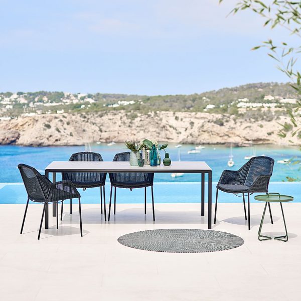 Image of black Breeze modern garden chairs with Cane-line black outdoor table on terrace with sea and headland in background