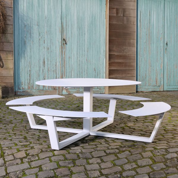 Image of La Grande Ronde circular picnic table in white, shown on cobbled stone floor with old industrial building in the background