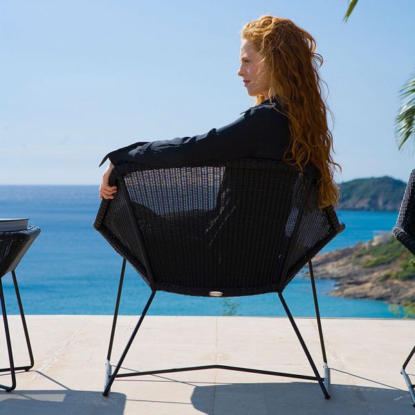 Image of red headed woman sat in black Breeze garden easy chair by Cane-line, with inviting sea in the background