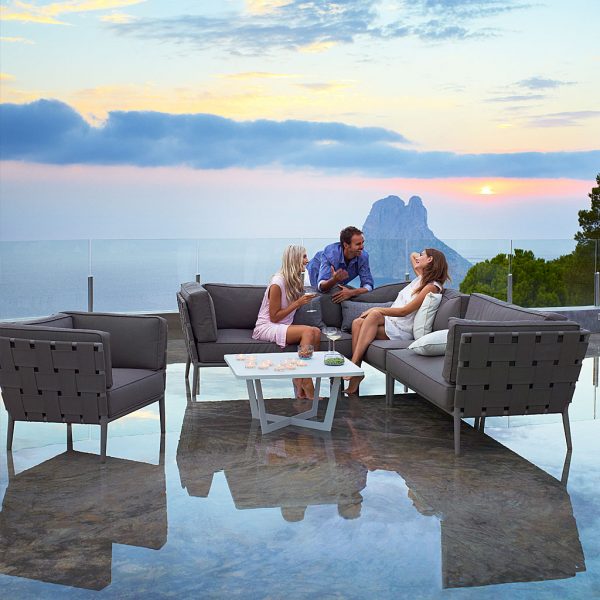 Image of 3 people chatting and laughing on Conic luxury outdoor sofa by Cane-line, with setting sun in background