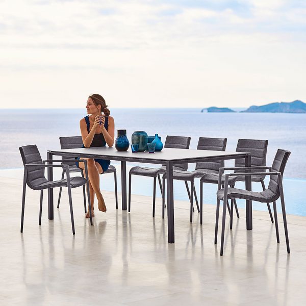 Image of woman sat in Core garden chair next to Pure outdoor dining table by Cane-line