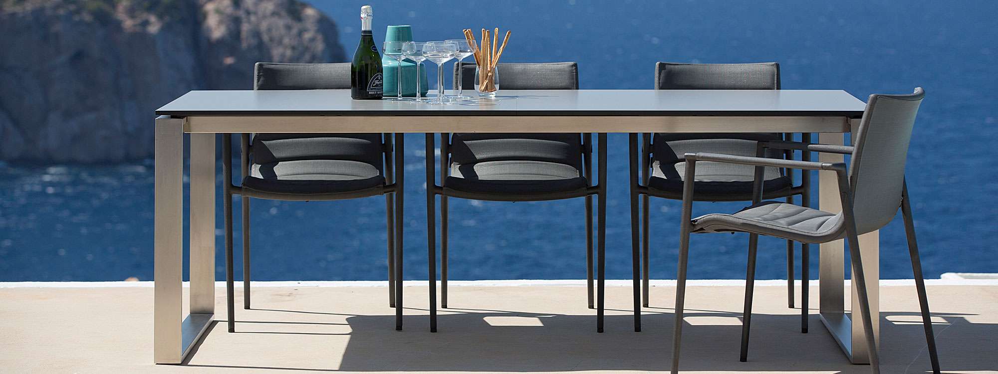 Image of Core garden chairs around Cane-line dining table on terrace, with sea and cliffs in background