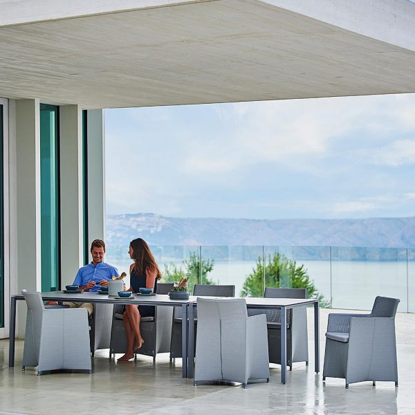 Image of couple sat on Diamond garden chairs next to Caneline Pure dining table, shown on terrace beneath cantilevered balcony