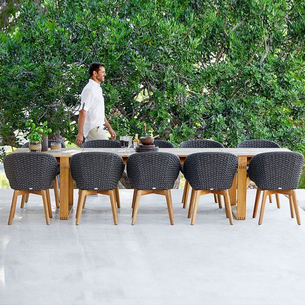 Image of man walking behind Endless long teak table and Peacock tub garden chairs by Cane-line