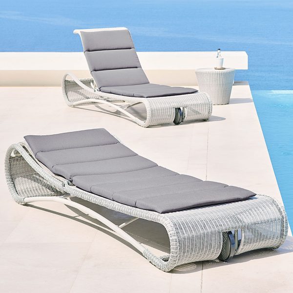 Image of pair of white-grey rattan Escape sun loungers and Kingston rattan side table by Cane-line, next to swimming pool with sea in the background