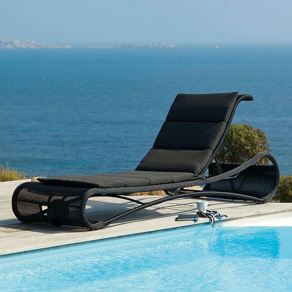 Image of black Escape sun lounger with black cushion by Cane-line, on poolside with sea disappearing into the distance behind