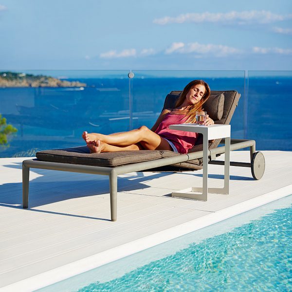 Image of woman relaxing in Cane-line Conic adjustable sunbed next to Time Out cantilever side table on poolside