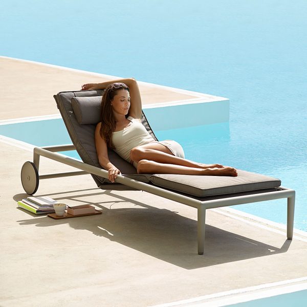 Image of woman lying in Conic modern sun lounger by Cane-line, next to inviting swimming pool