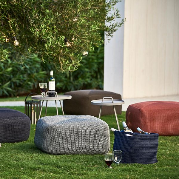 Image of Cane-line Divine garden poufs in different colors around On The Move tray tables, shown on verdant green lawn