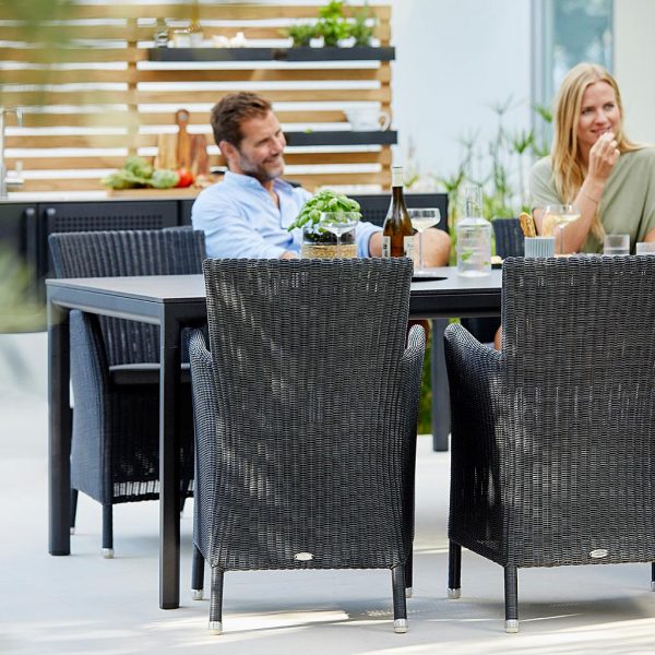 Image of couple sat in black Hampsted rattan garden chairs around Pure black outdoor table by Cane-line