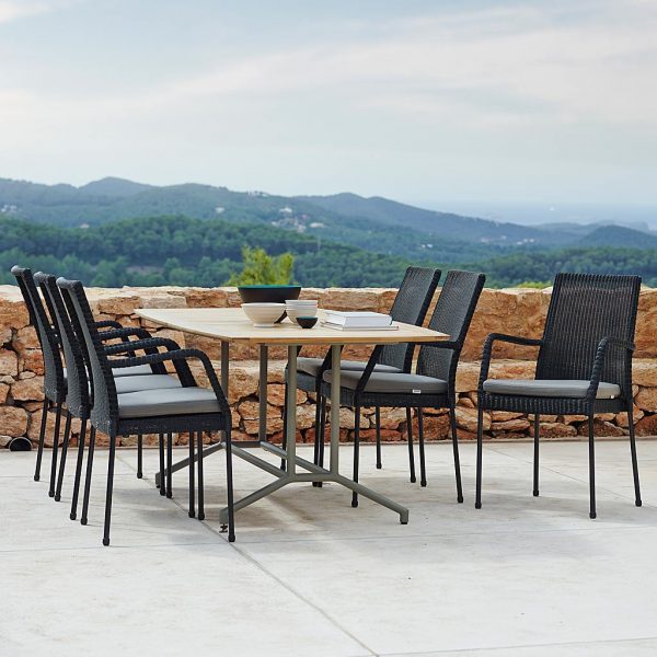 Image of Caneline Newport stacking garden chairs and teak dining table, with drystone wall and hills beyond