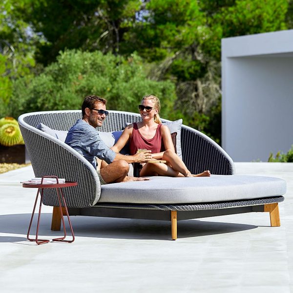 Image of man and woman lying back relaxing in Caneline Peacock luxury garden daybed on chic poolside