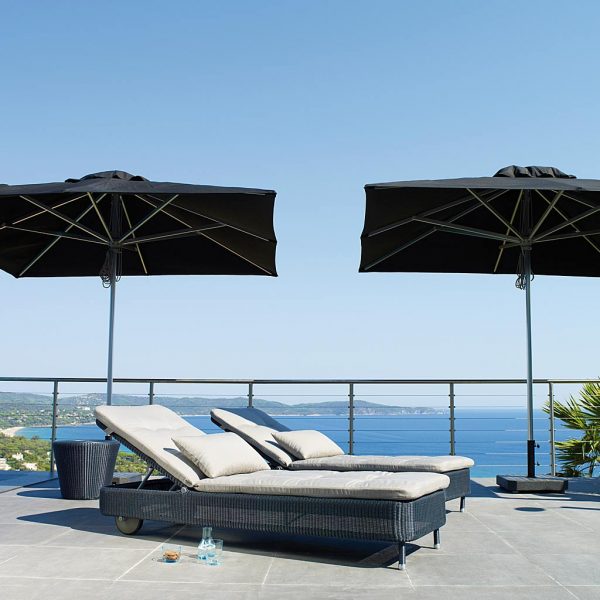Image of pair of Presley graphite rattan sun loungers on terrace, beneath 3 black Cane-line parasols