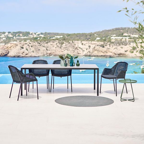 Image of Breeze woven rattan garden chairs and Pure outdoor table by Cane-line, with bay and sea in the background