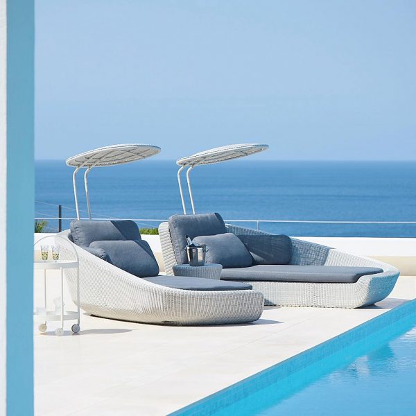 Image of Cane-line Savannah white rattan daybeds with grey cushions, on minimalist poolside with sea in background