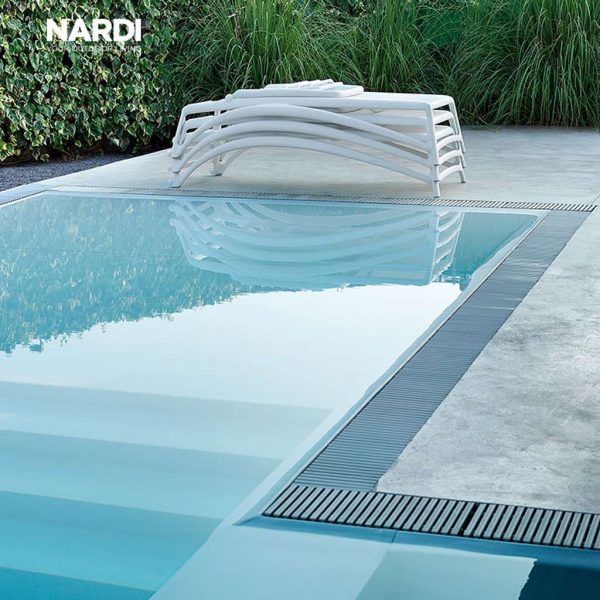 Image of Stacked White ATLANTICO Contract SUN LOUNGERS by Nardi, with swimming pool in foreground at dusk
