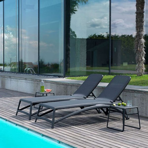 Image of pair of Atlantico black contract sun loungers with Pop side table by Nardi, shown on wooden-decked poolside with floor to ceiling glass in the background