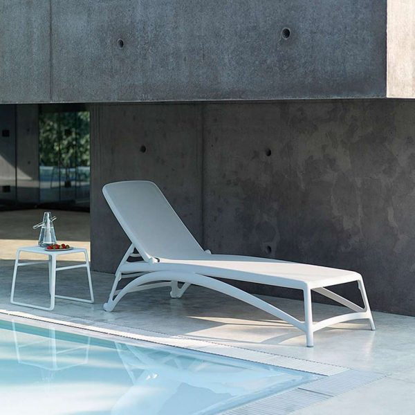 Image of Atlantico white modern plastic sun lounger and white Pop side table by Nardi, shown in minimalist poolside