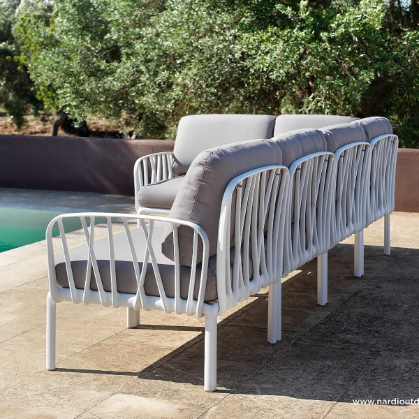 Image of side and back of Komodo white modular garden sofa with taupe cushions, shown on poolside in the sun