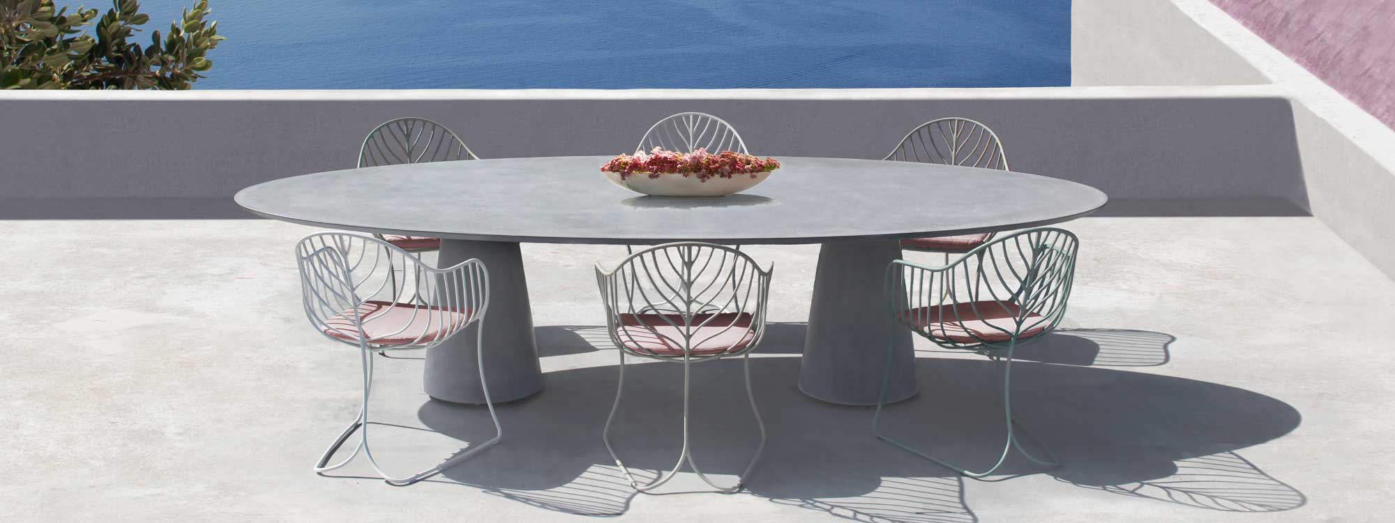 Image of Conix concrete garden table & white Folia chairs by Royal Botania on terrace overlooking azure sea.