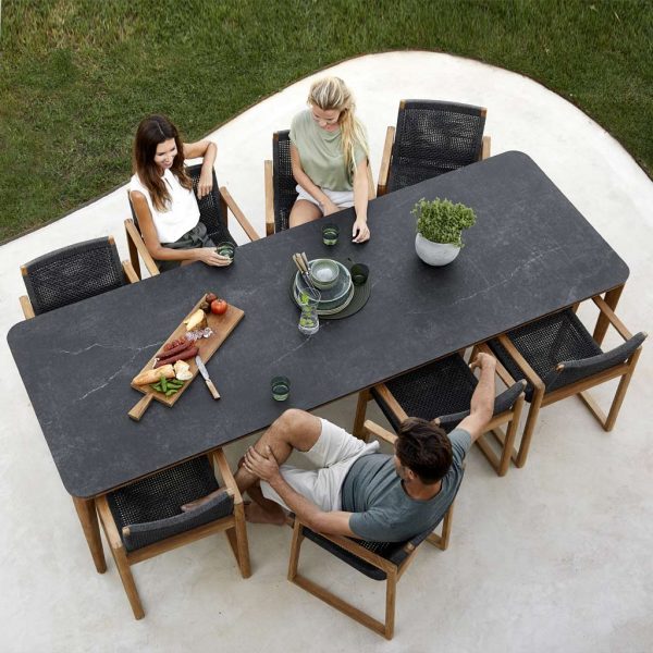 Image of birds eye view of Caneline teak table and its fossil black ceramic table top, shown on terrace with Endless teak carver chairs with dark-grey woven seat and back