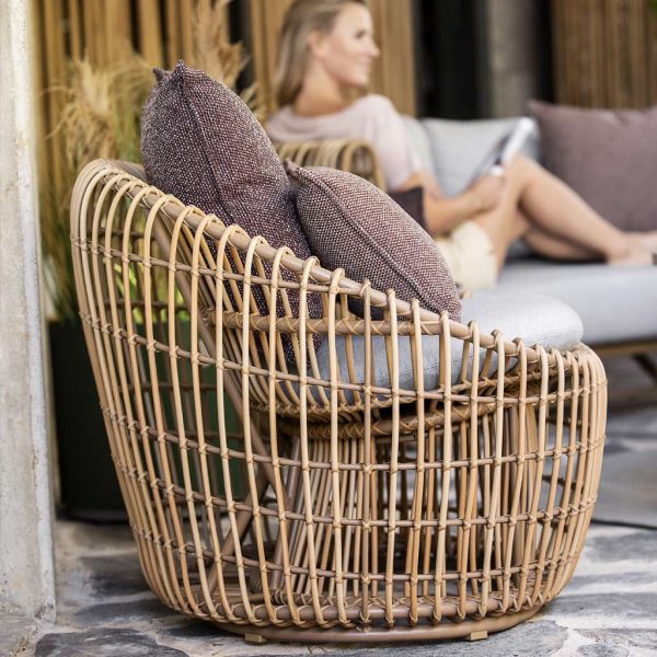 Image of round Caneline Nest lounge chair in natural Cane-line Weave with taupe cushions, with woman reading in background