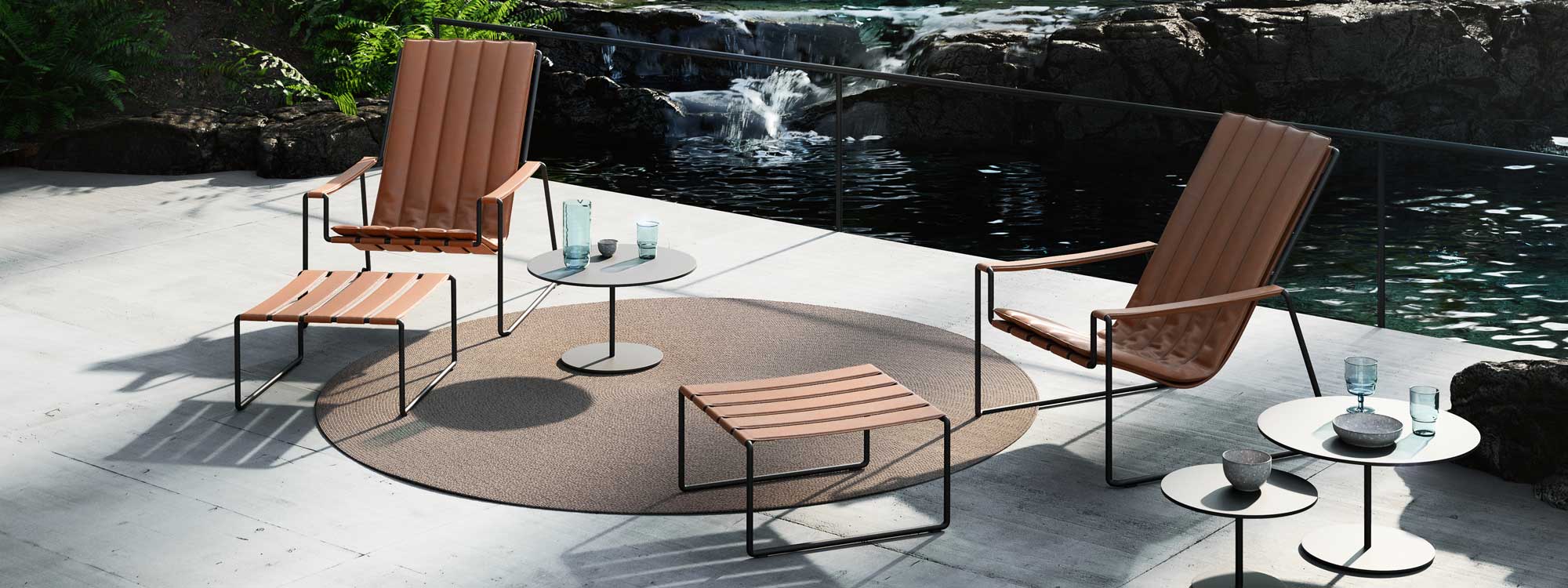 Image of Royal Botania Butler garden low tables & Strappy easy chairs on poured concrete terrace with tranquil water feature in the background