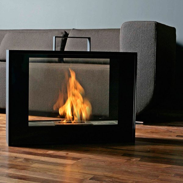 Image of flames dancing within Conmoto Travelmate portable fireplace, situated on polished wooden floor with minimalist brown sofa in background