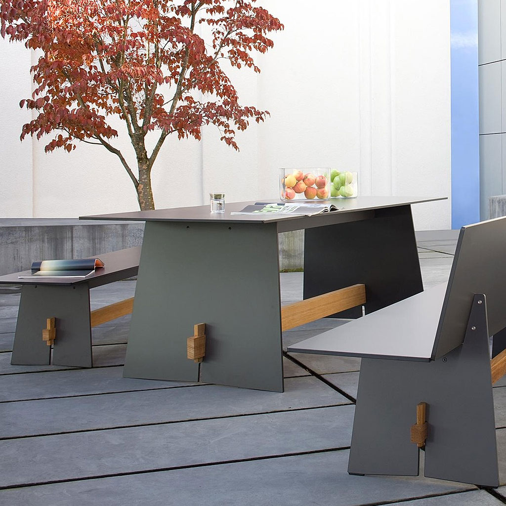 Image of Tension modern garden table and benches in grey HPL and iroko hardwood, with modern architecture and Acer tree in the background
