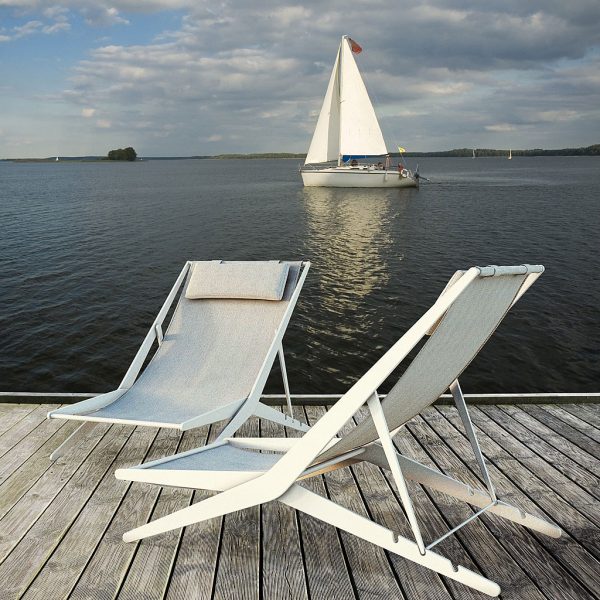 Pair of white Boomy folding deck chairs on wooden decking with yacht in background