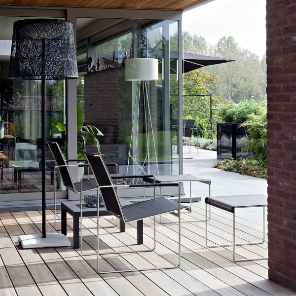 Image of pair of FueraDentro Poltrona minimalist garden lounge chairs and foot stools in EP stainless steel and black Batyline, shown on wooden decked terrace looking out over a garden