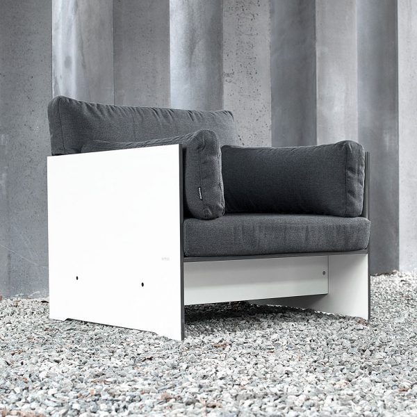 Image of Conmoto Riva white garden lounge chair with anthracite cushions, shown on gravel floor with concrete structure in the background