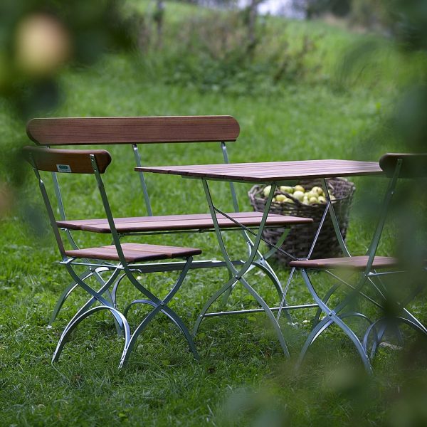 Image of Brewery traditional folding garden table, chairs and bench in galvanised steel and teak by Grythyttan, shown in long grass in a meadow.