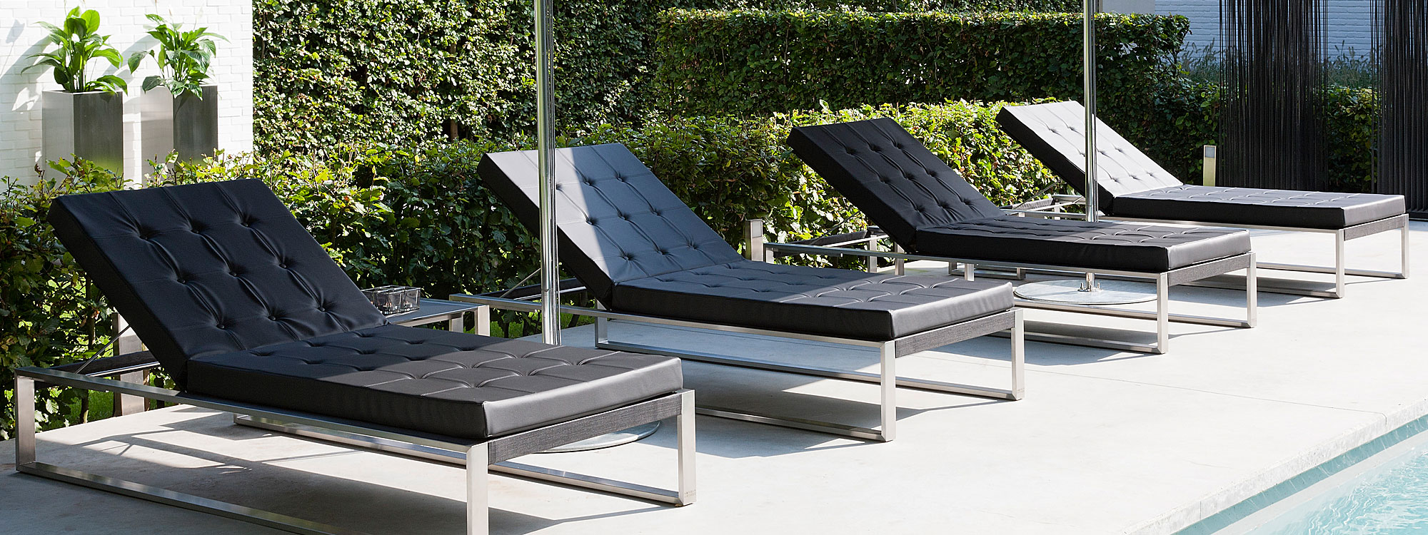 Image of row of 4 Siesta minimalist sun loungers with brushed stainless steel frames, black Batyline seat and back and black Stamskin cushions