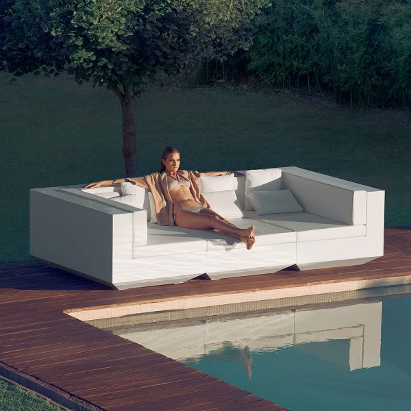 Image of woman lying back in large white Vela garden sofa by Vondom on sunny poolside