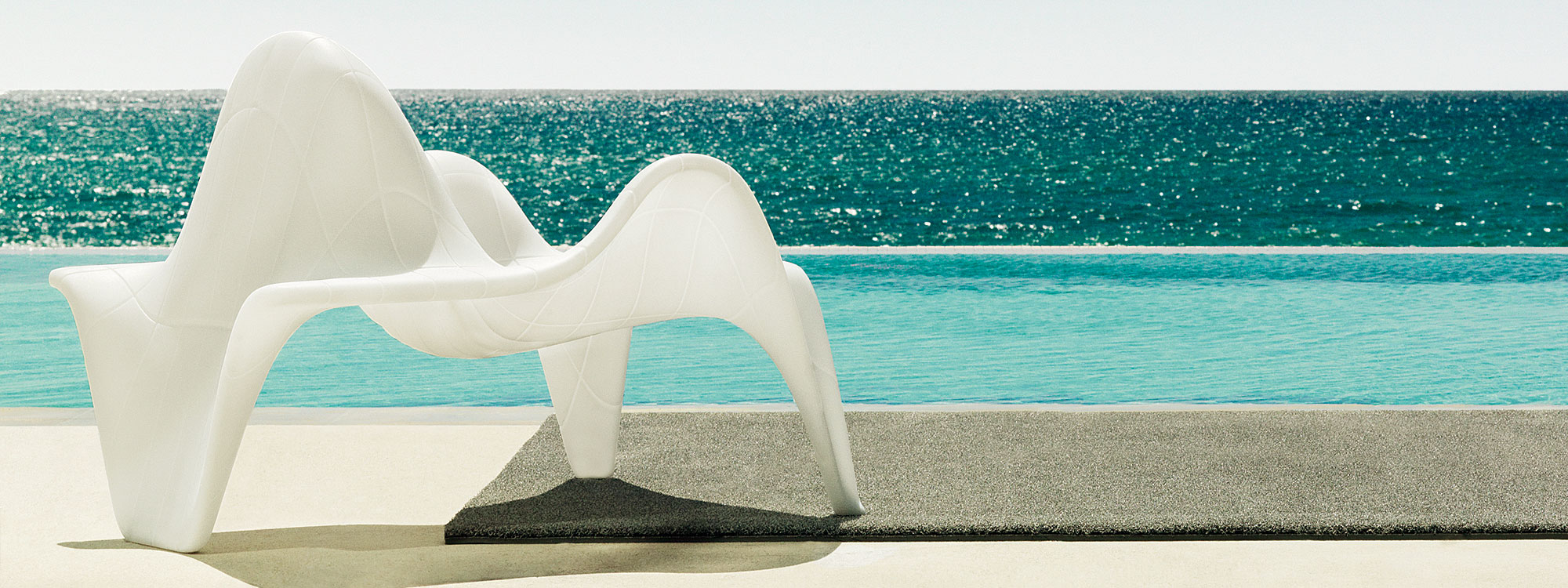 Image of Vondom F3 modern outdoor lounge chair in white roto-molded polyethylene with swimming pool, blue sea and sky in the background