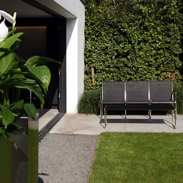 Image of FueraDentro Poltrona 3 minimalist garden sofa seat, shown against a green hedge next to a whitewashed wall