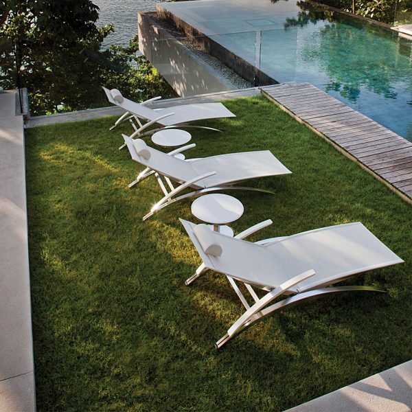 Image of row of 3 white OZON sunbeds and side tables on grassy poolside