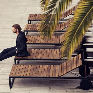 Dude in black suit sitting n end of Roshults teak and stainless steel sun lounger