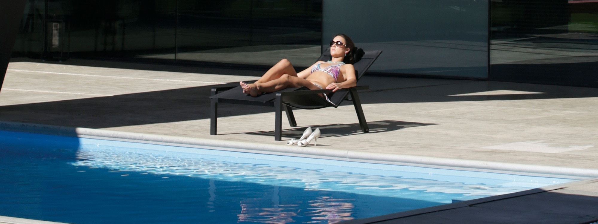 Image of woman relaxing in black Alura sun lounger by Royal Botania beside swimming pool