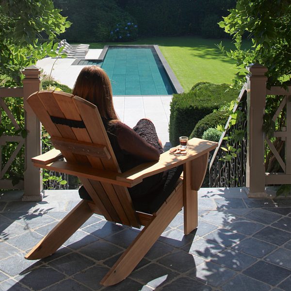 Image of woman relaxing in New England teak lounge chair by Royal Botania on veranda with swimming pool in garden below