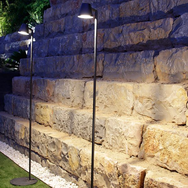 Nighttime image of pair of illuminated Royal Botania Parker outdoor standard lamps against a stone wall