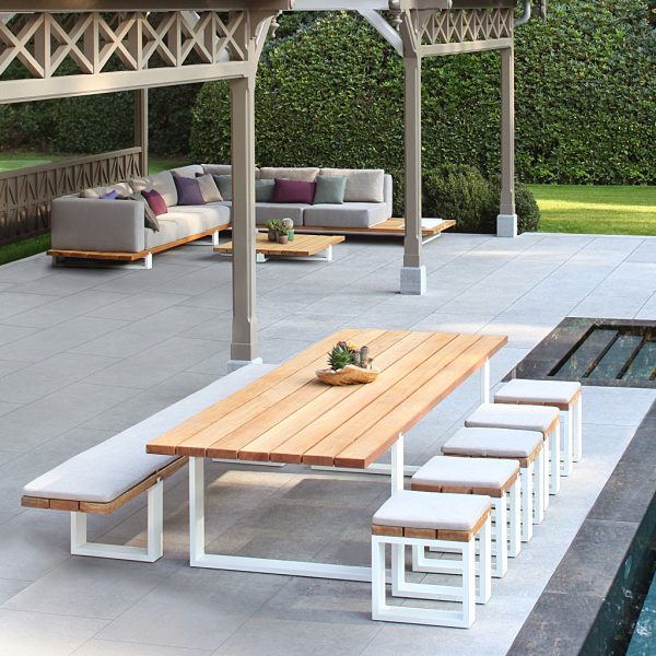 Image of Royal Botania Vigor teak table and benches with white frames, set between swimming pool and summer house